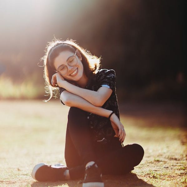 Smiling woman stretching outdoors in a green park with sunlight.